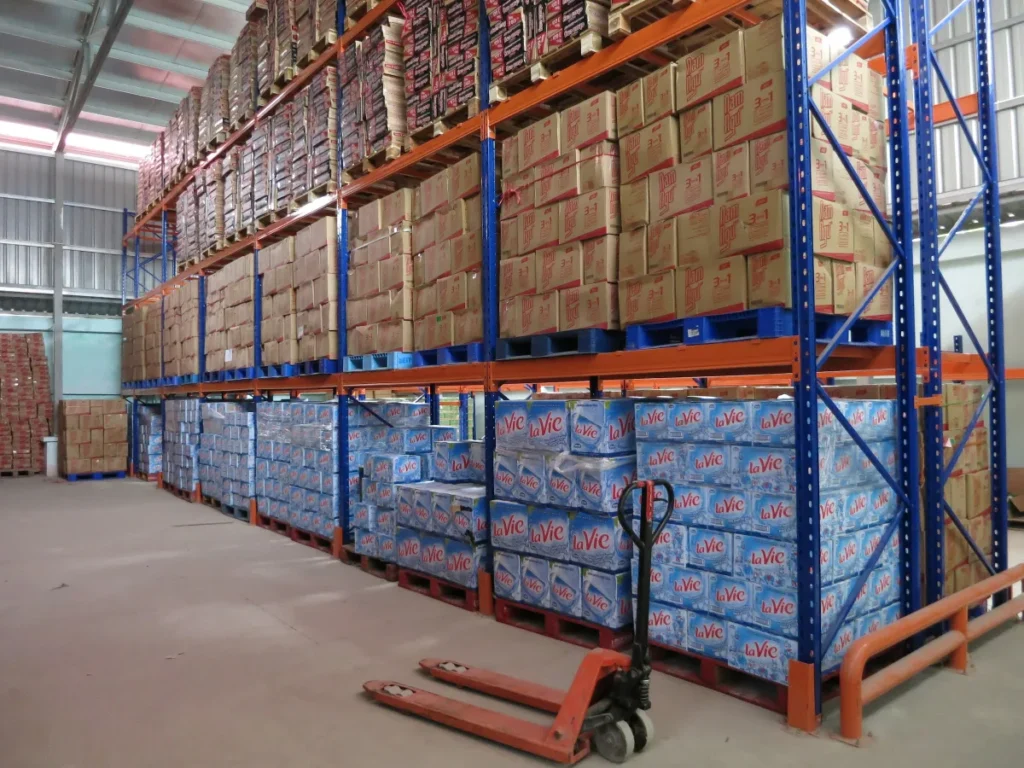 Xe nâng tay đặt trong lối đi giữa các dãy kệ pallet Selective chứa hàng Xe nâng tay đặt trong lối đi giữa các dãy kệ pallet Selective chứa hàng